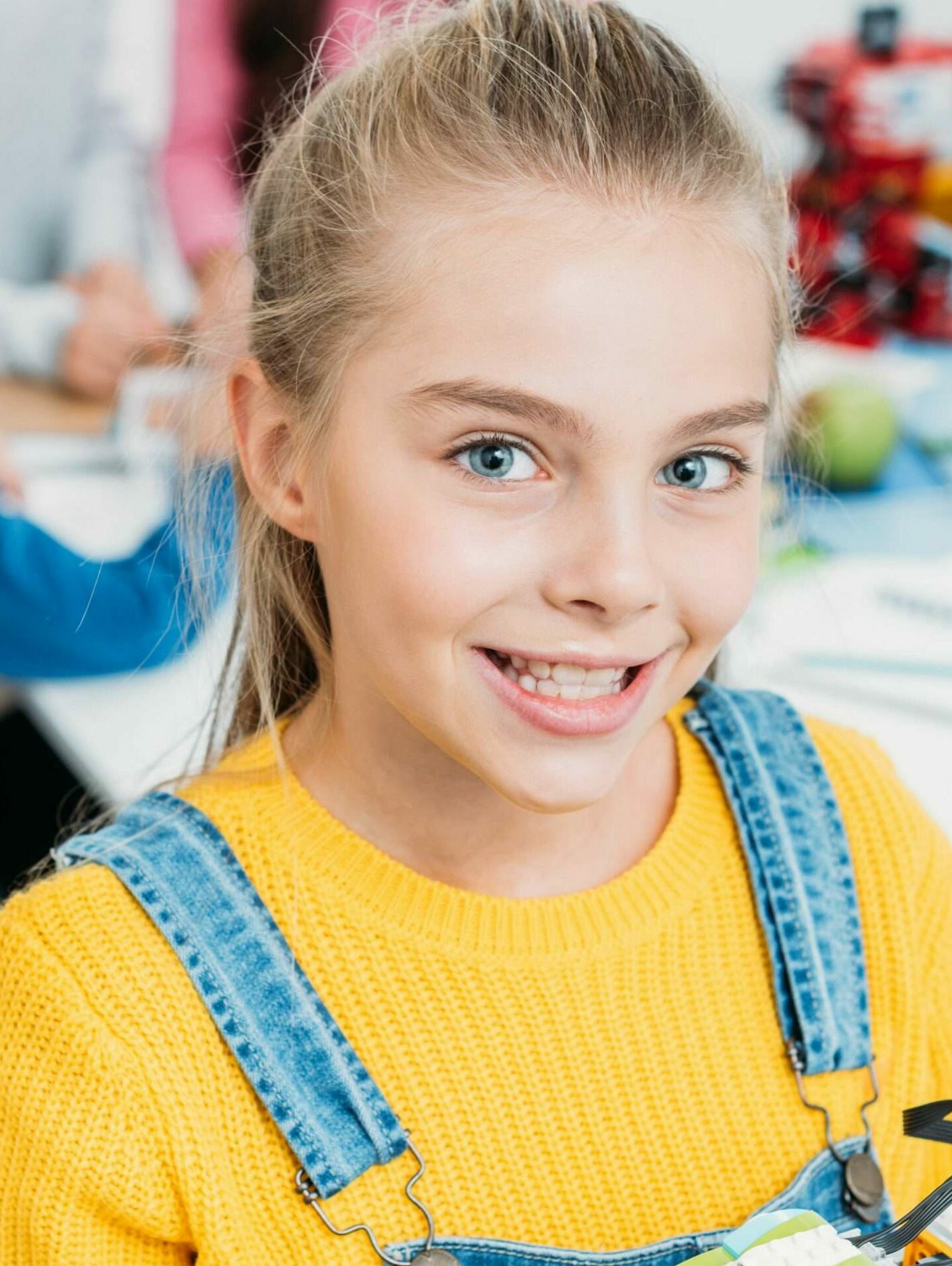 preteen schoolgirl holding multicolored robot and looking at camera in classroom